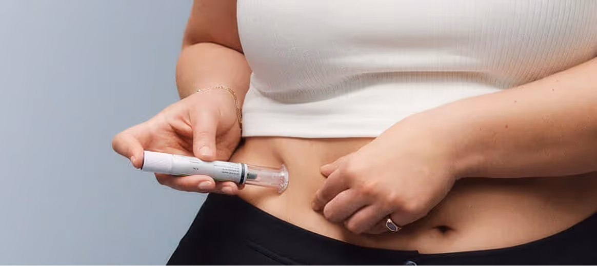 Person using a white insulin pen to inject medication into their abdomen.
