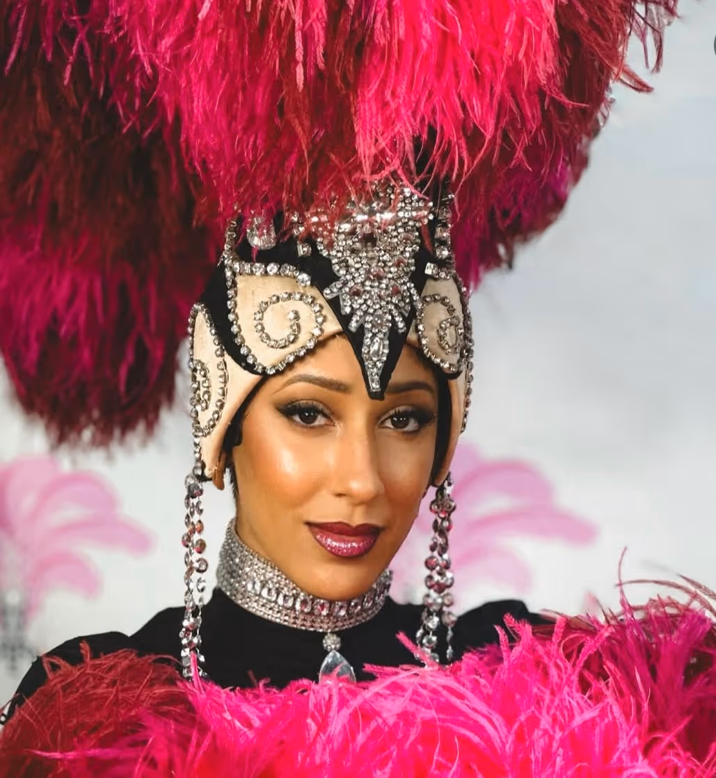 Woman wearing an ornate headdress with pink feathers and sparkling jewelry on chin and neck at Showgirl Bootcamp Experience in Las Vegas.