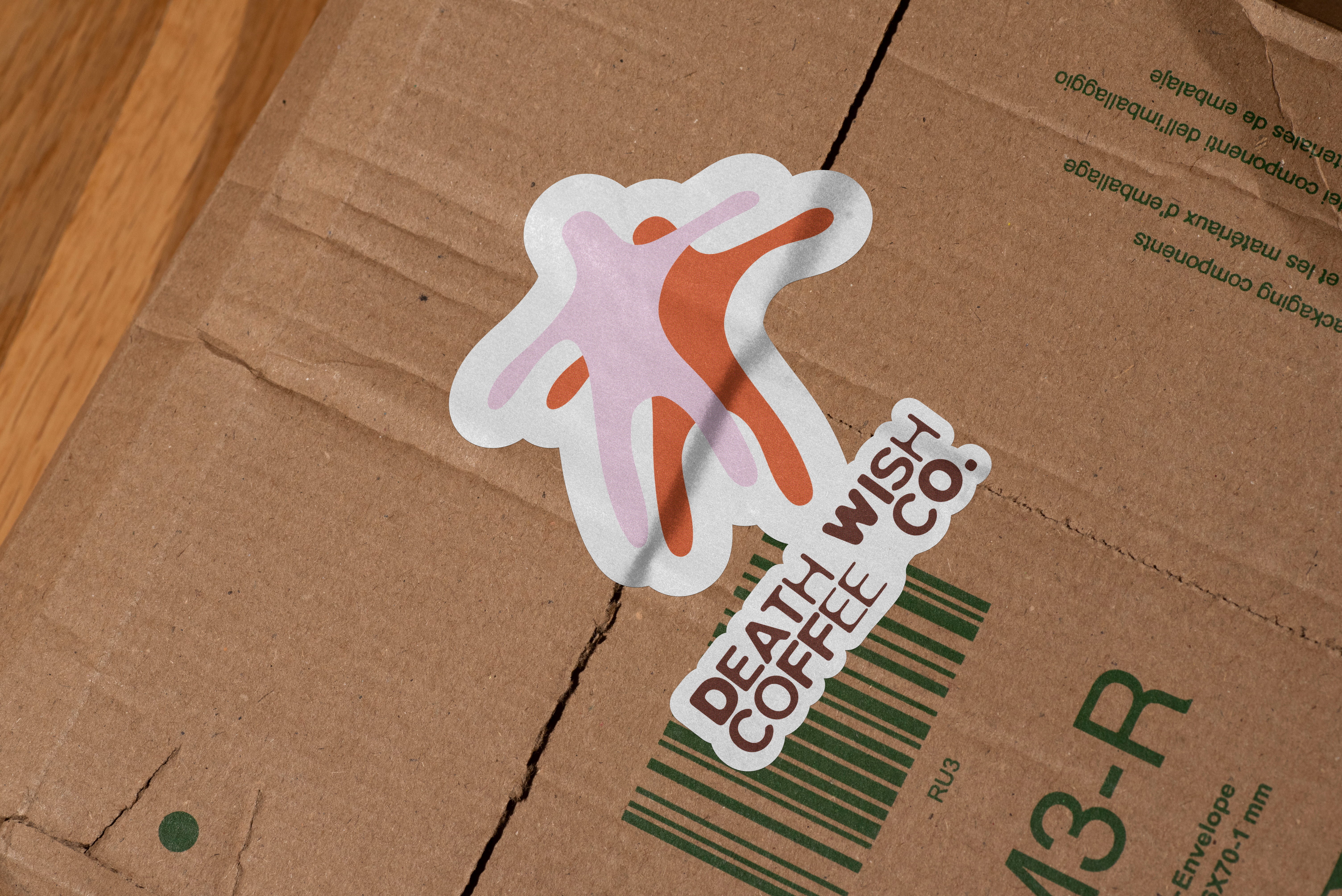 mockup found on magnific -Sticker on cardboard box featuring two stylized dancing figures in pink and orange with text Death Wish Coffee Co.