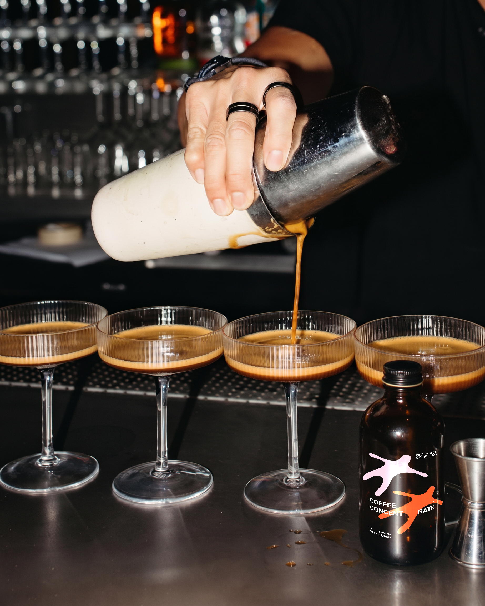 image generated by magnetic AI - Hand pouring espresso martini cocktail from shaker into glass among four glasses in a row at bar.