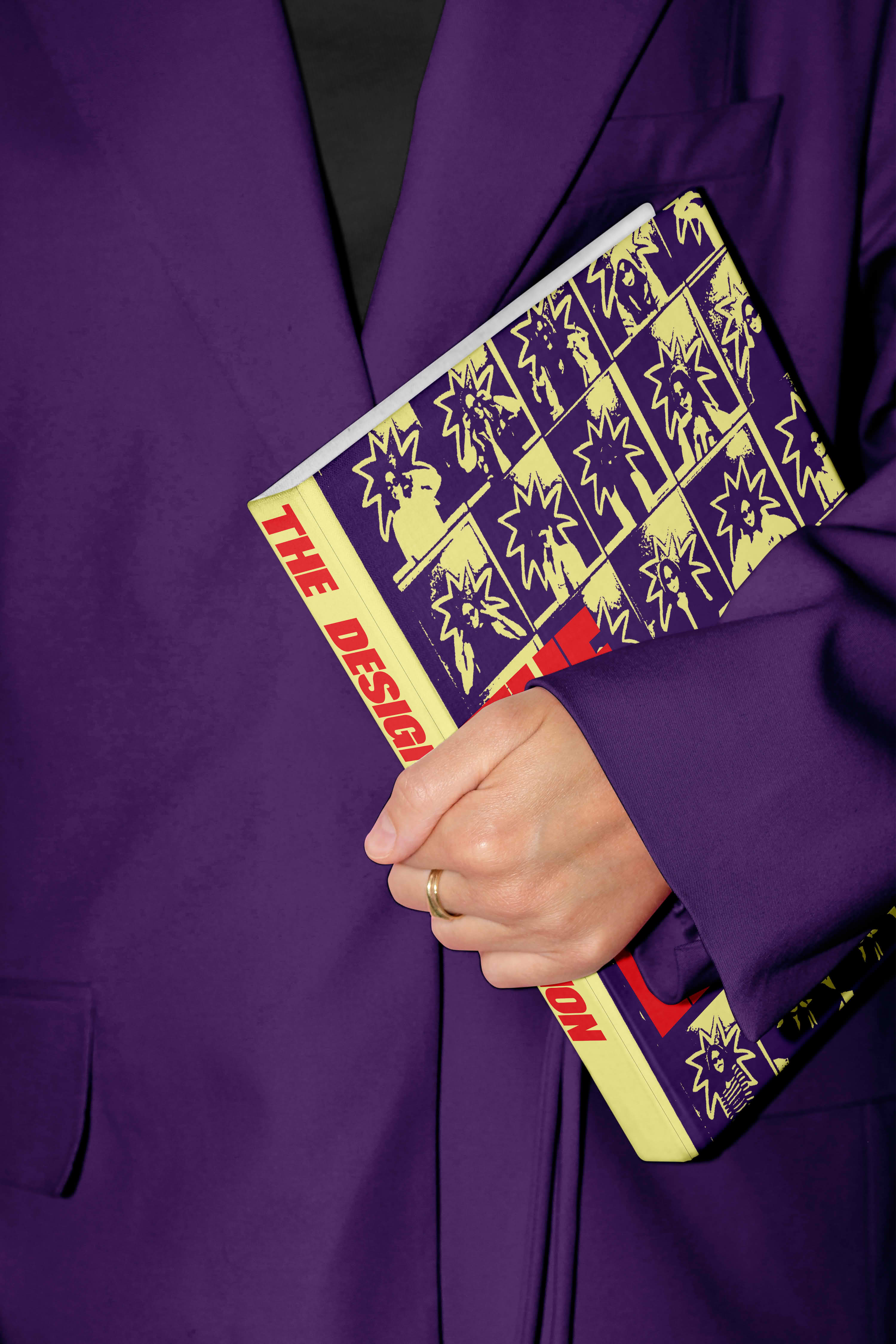 mockup found on magnific -Hand with wedding ring holding a book titled 'The Design' against a purple blazer.