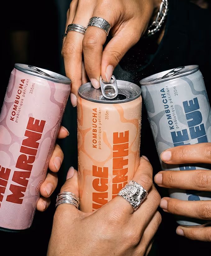 image generated by adobe firefly -Three hands holding and opening colorful kombucha cans with bold text labels against a dark background.