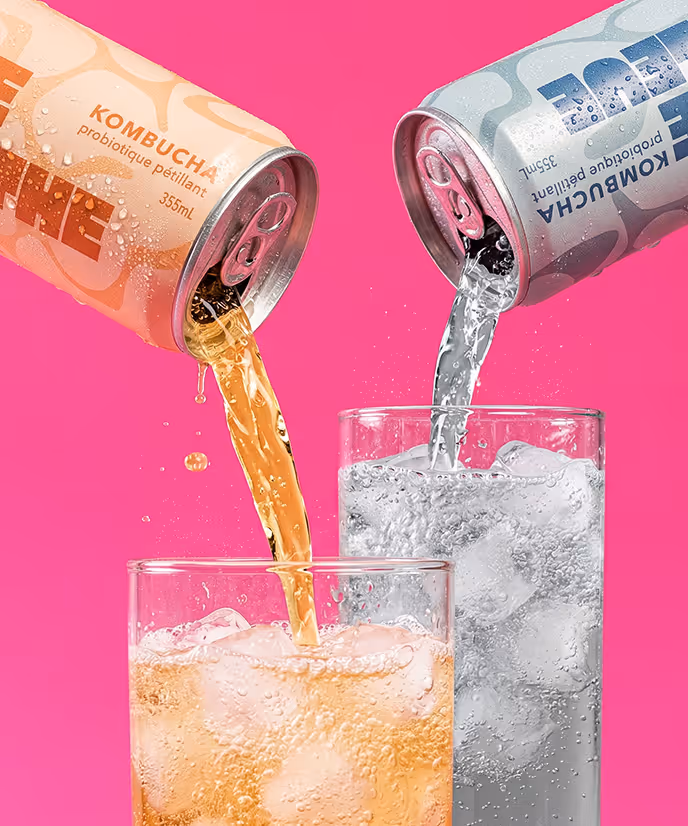 image generated by adobe firefly -Two kombucha cans pouring fizzy drinks into glasses filled with ice against a pink background.