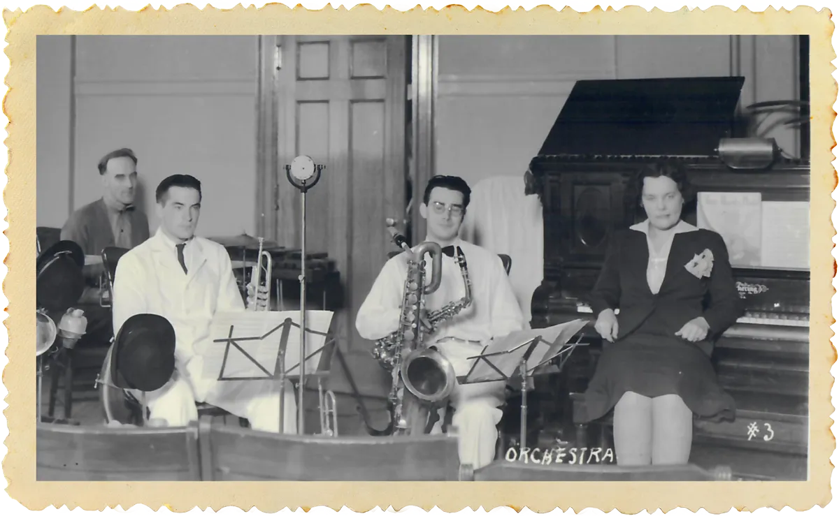 Black and white photo of four musicians seated with instruments: piano, saxophone, trumpet, and drums.