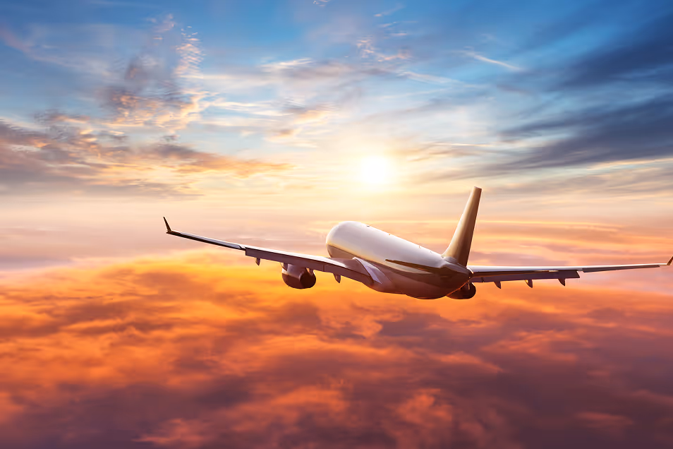 Airplane flying above clouds at sunset with a colorful sky and sun in the background.