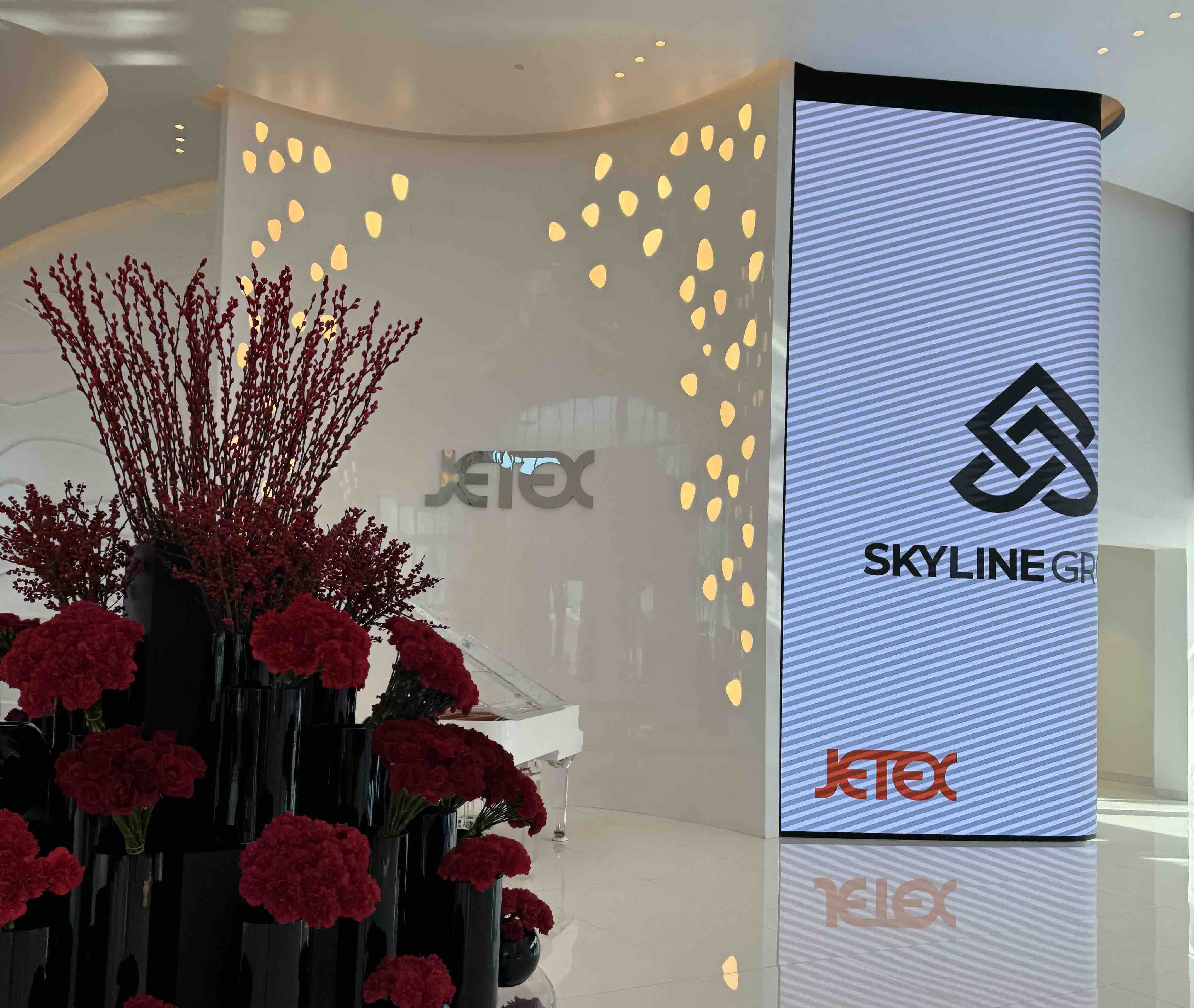 Modern white lobby with red flowers, abstract wall lights, and Skyline Group and Jetex logos displayed.