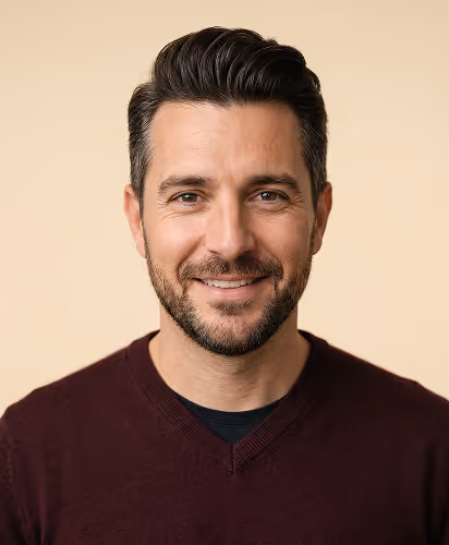 Smiling man with dark hair and beard wearing a maroon V-neck sweater against a beige background.