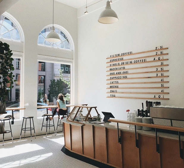 Bright modern café interior with wooden counter, stools, and coffee menu on the wall.