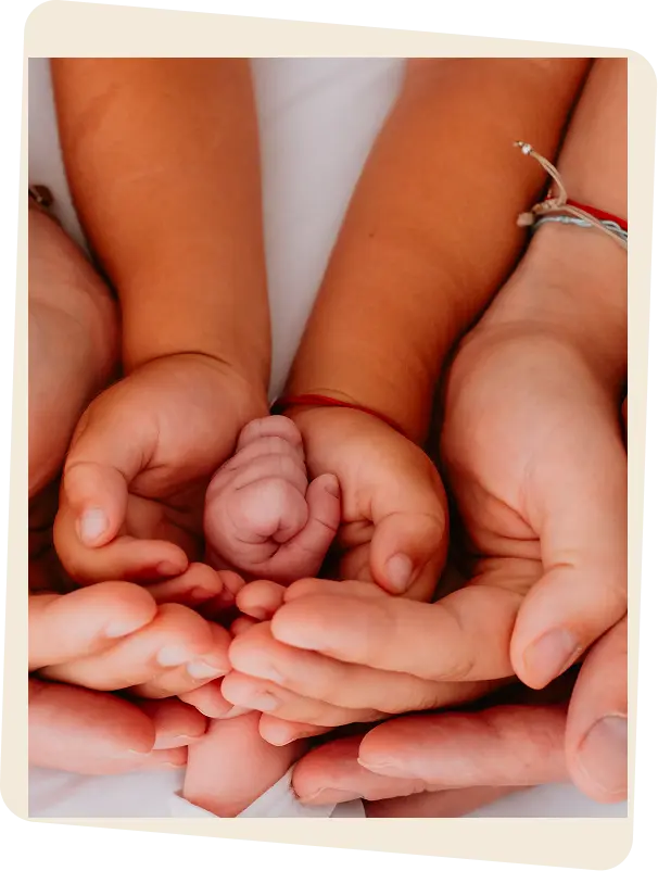 Familienhände halten die Hand eines Neugeborenen, Wochenbettbetreuung bei In Hebammenhänden