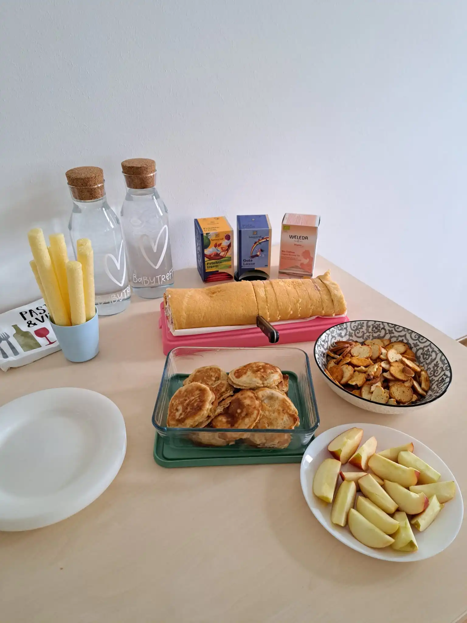 Gedeckter Tisch mit Snacks beim Baby-Treff: Pfannkuchen, Obst, Knabbereien und Tee