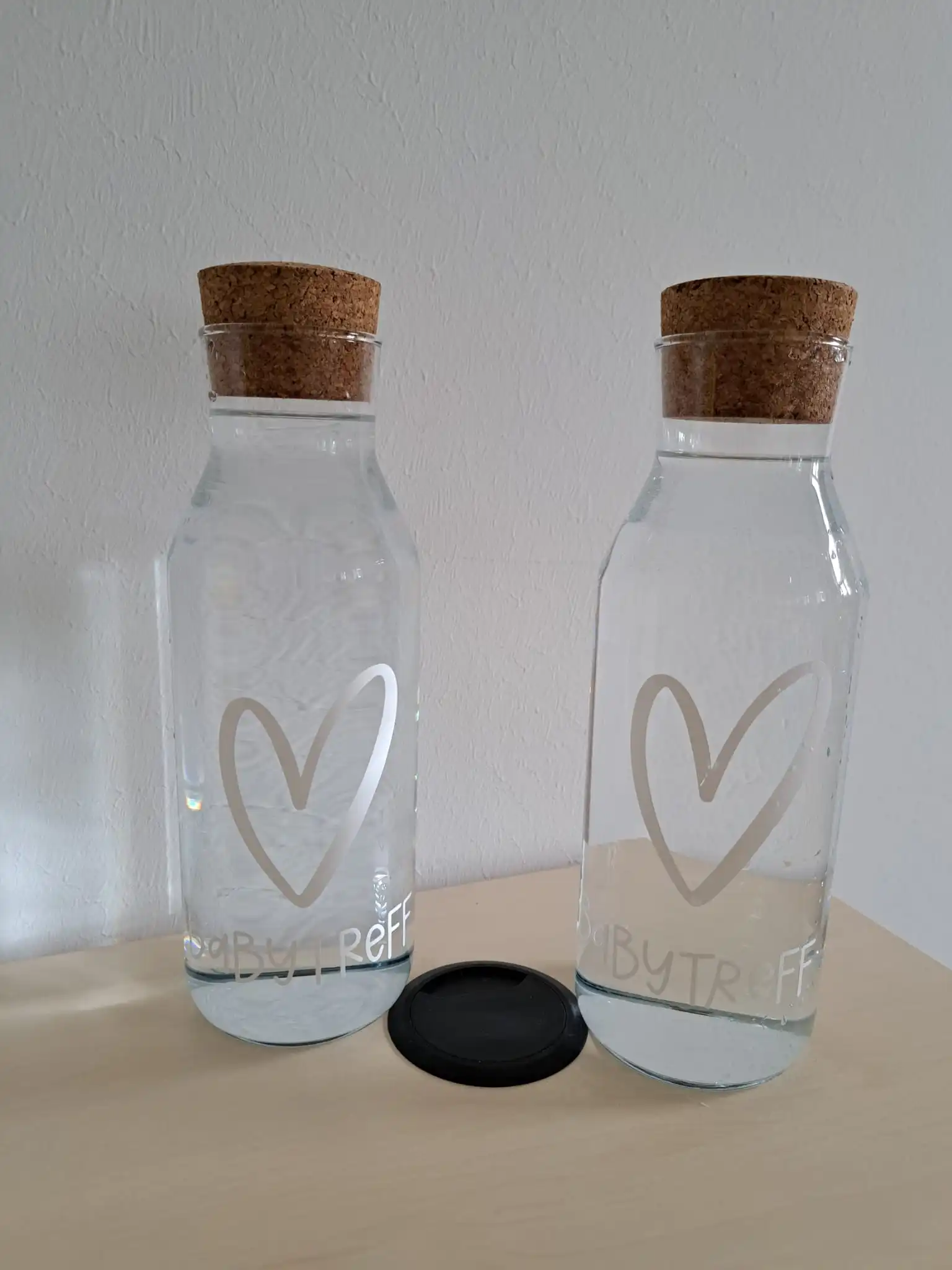 Zwei Wasserkaraffen mit Herz und Schriftzug Baby-Treff auf einem Tisch