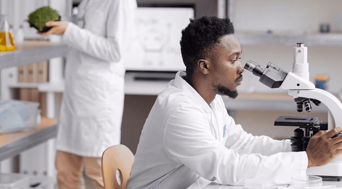 Man in a lab coat examining a sample through a microscope in a laboratory setting.