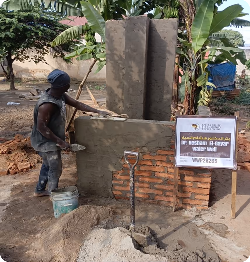 A worker in progress building the concrete well head for the Dr. Hesham El-Gayar Water Well, with the ARCD dedication sign posted alongside.