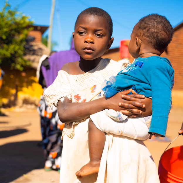 Young girl holding a small child in her arms while standing outdoors in a residential community.