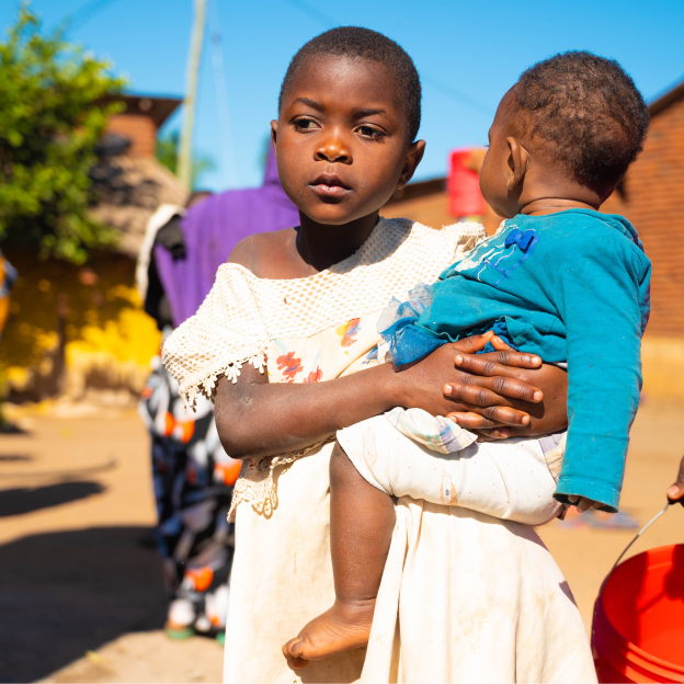 Young girl holding a small child in her arms while standing outdoors in a residential community.