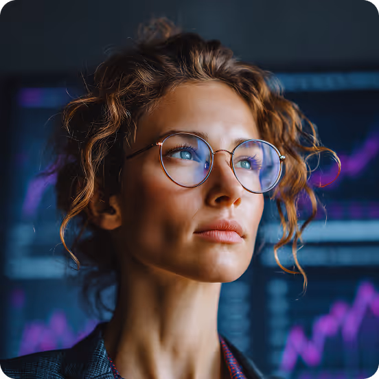 Young woman with curly hair and glasses looking away, with blurry financial charts in the background.