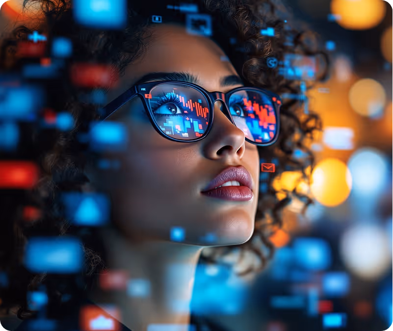Woman with curly hair wearing glasses reflecting digital graphs and data symbols in blue and red.