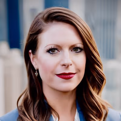 Portrait of a woman with brown wavy hair, red lipstick, and earrings, wearing a blue outfit.