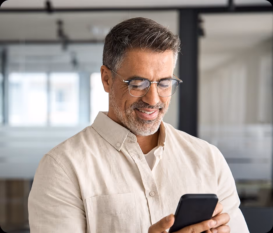 Smiling middle-aged man with glasses looking at his smartphone in a bright modern office.