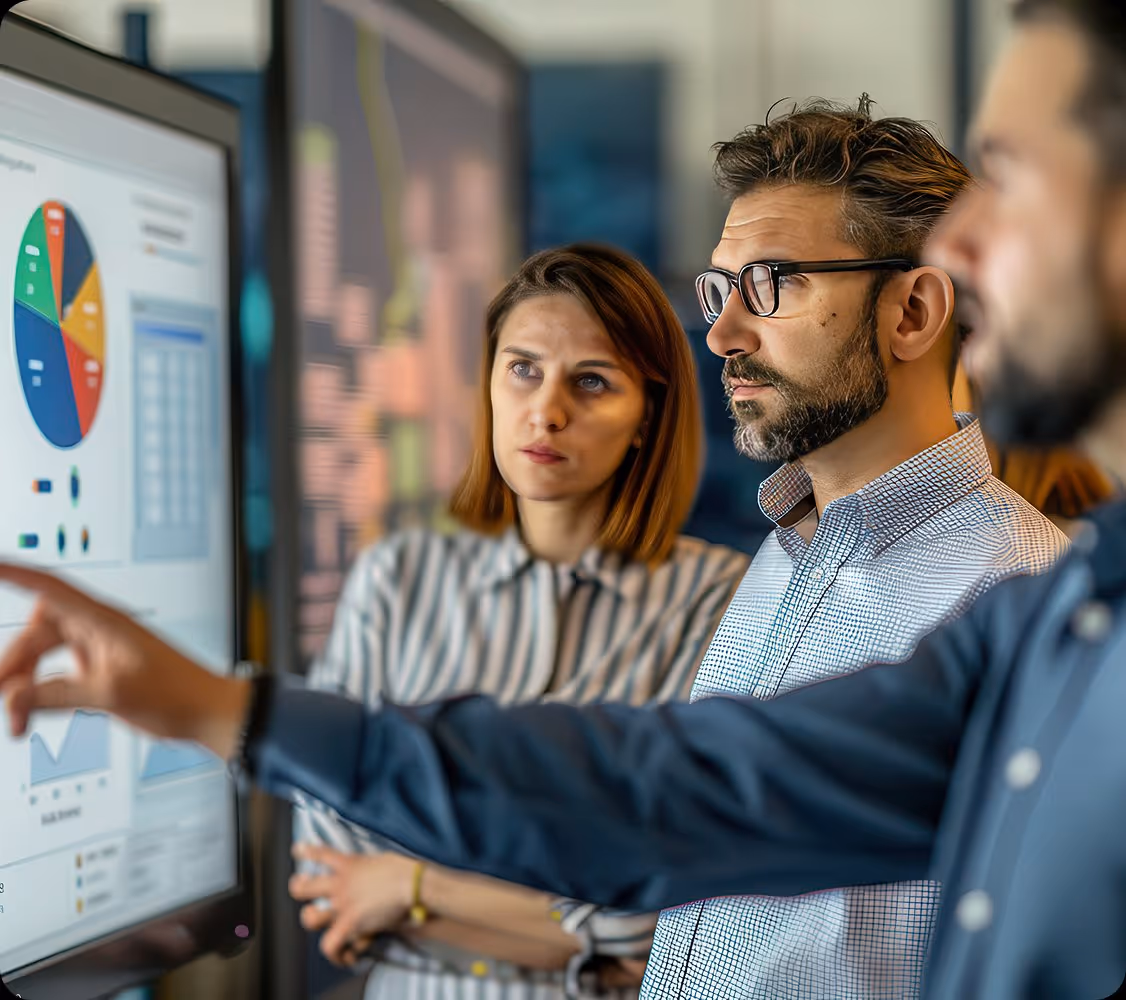 Three professionals focused on a digital display with charts and graphs during a discussion.