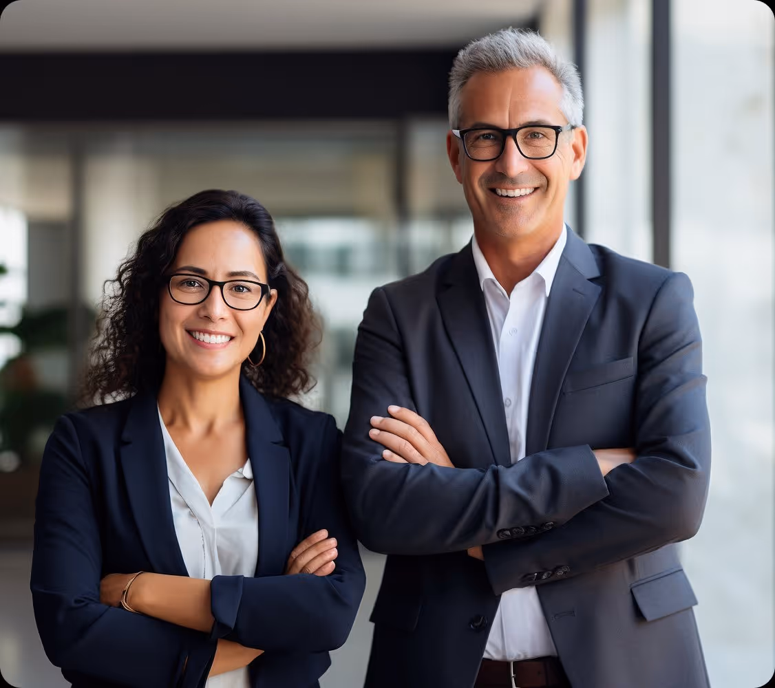 Smiling confident businesswoman and businessman standing with arms crossed in office.