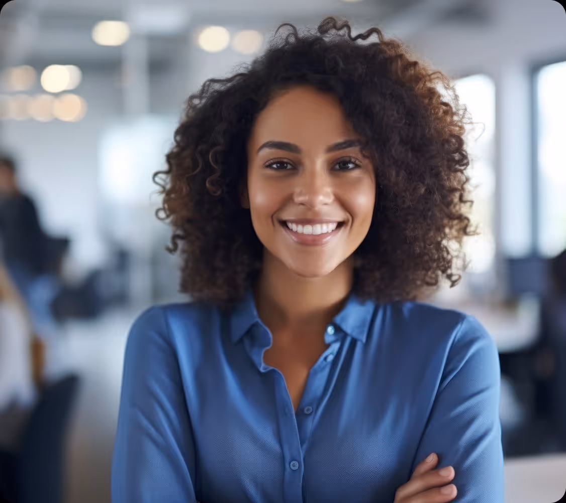 Smiling woman with curly hair wearing a blue shirt in a modern office environment.