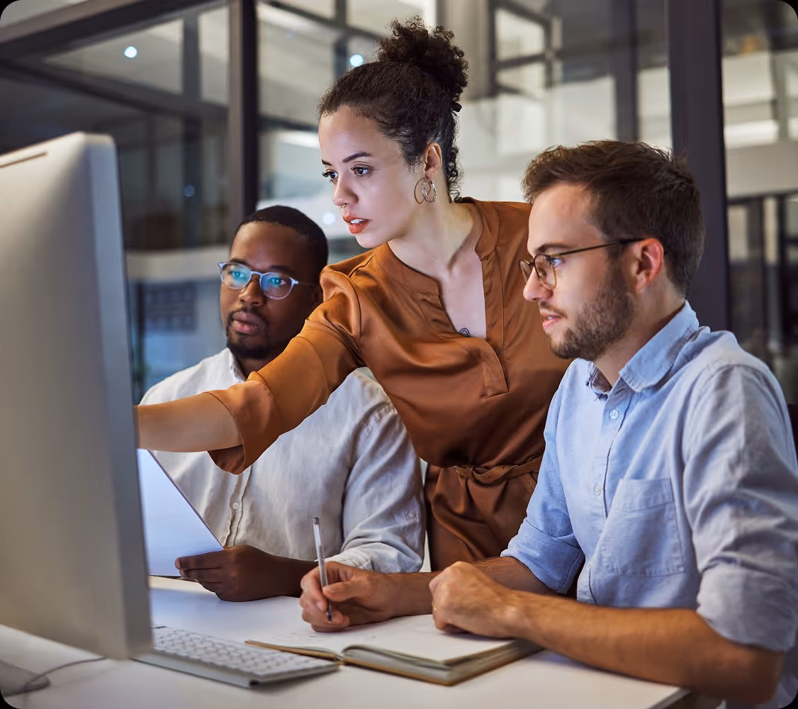 Three colleagues collaborating while looking at a desktop computer screen in a modern office.