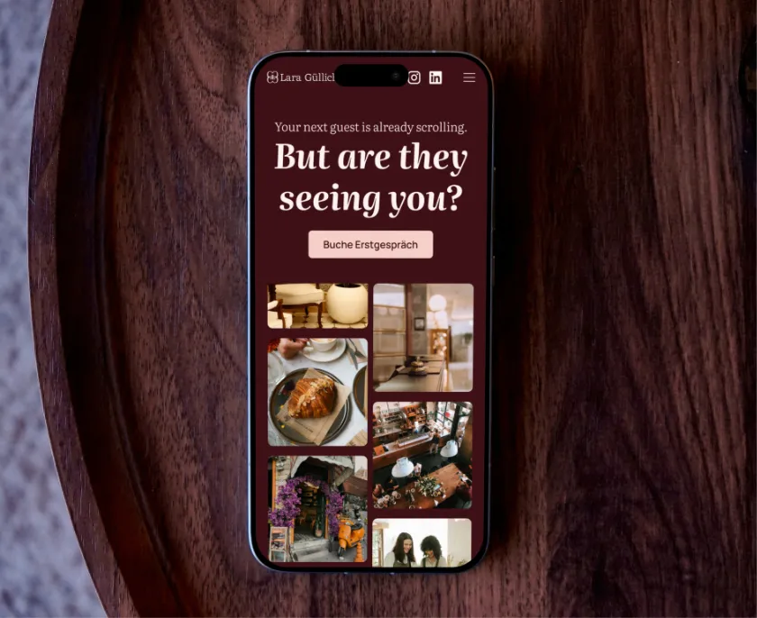 Smartphone auf einem Holztisch zeigt eine Website mit dem Text ‚Your next guest is already scrolling. But are they seeing you?‘ und einem Knopf ‚Buche Erstgespräch‘, darunter mehrere Bildausschnitte von Café- oder Restaurantmotiven.