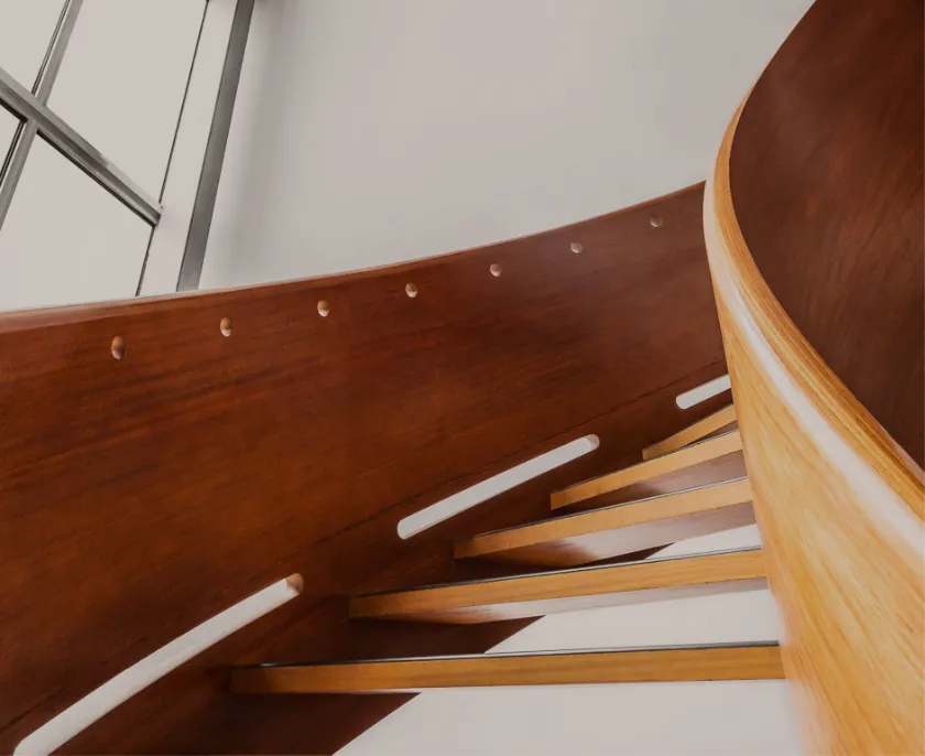 Abstrakte Aufnahme einer gewundenen Holztreppe mit glatt polierten Handläufen und Stufen aus hellem Holz vor weißer Wand.