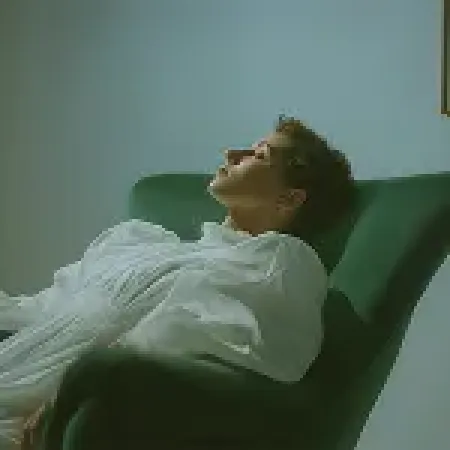 Person reclining in a green armchair with eyes closed in a calm, softly lit room.