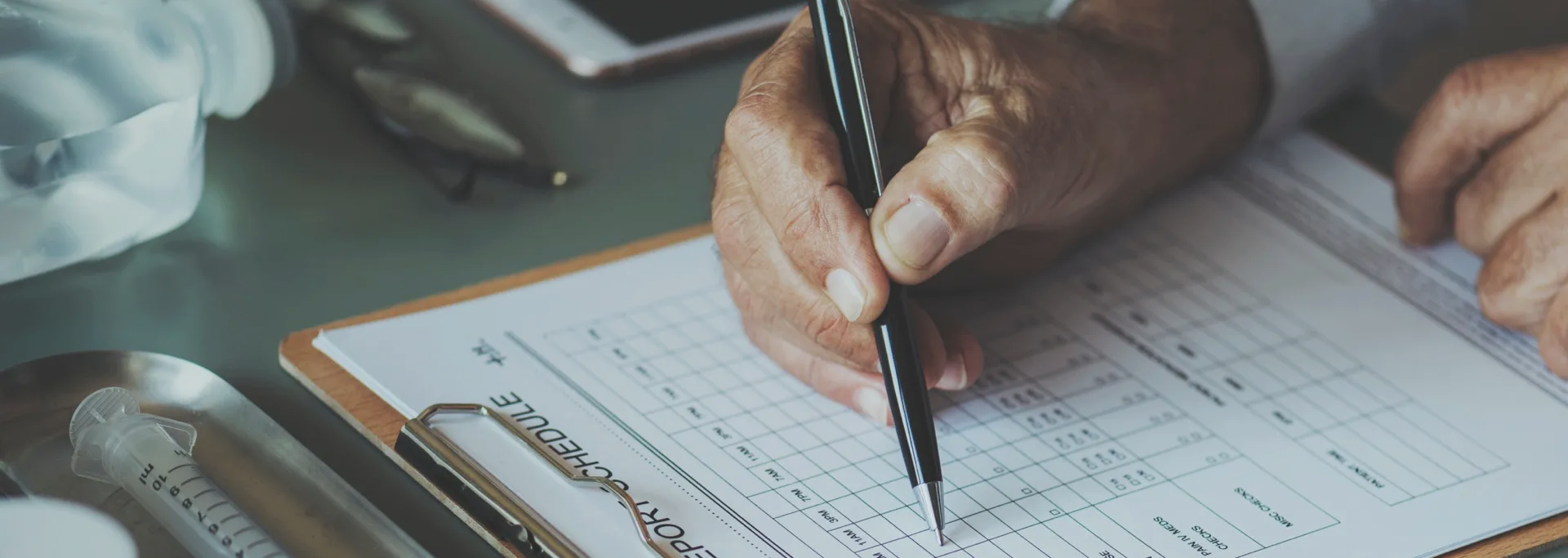 Close-up of a hand filling out a medical report form on a clipboard with a pen.