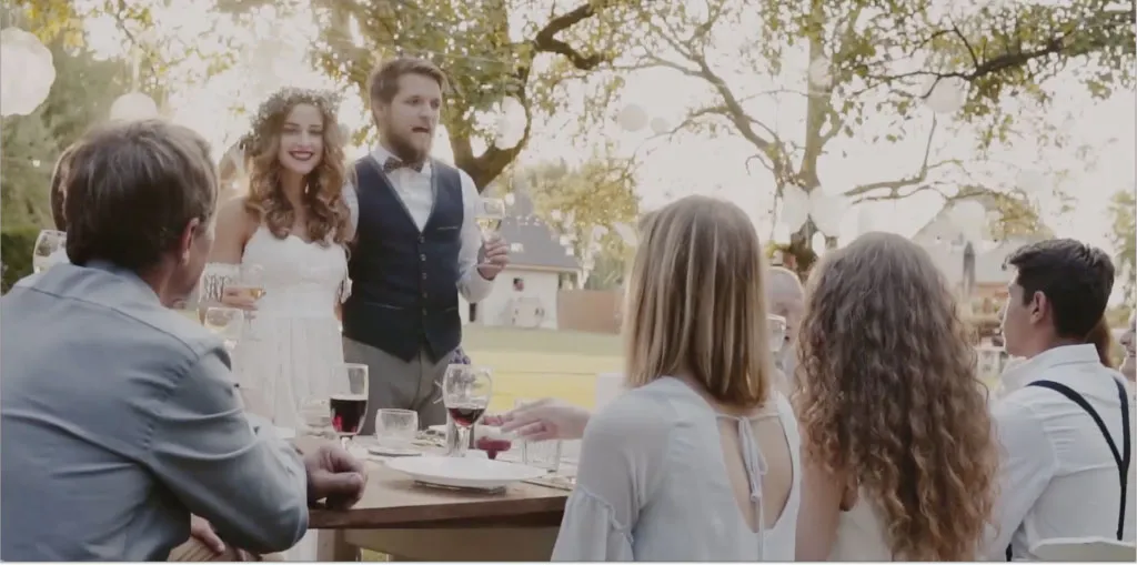 Bride and groom standing and toasting with guests seated at an outdoor wedding reception table.