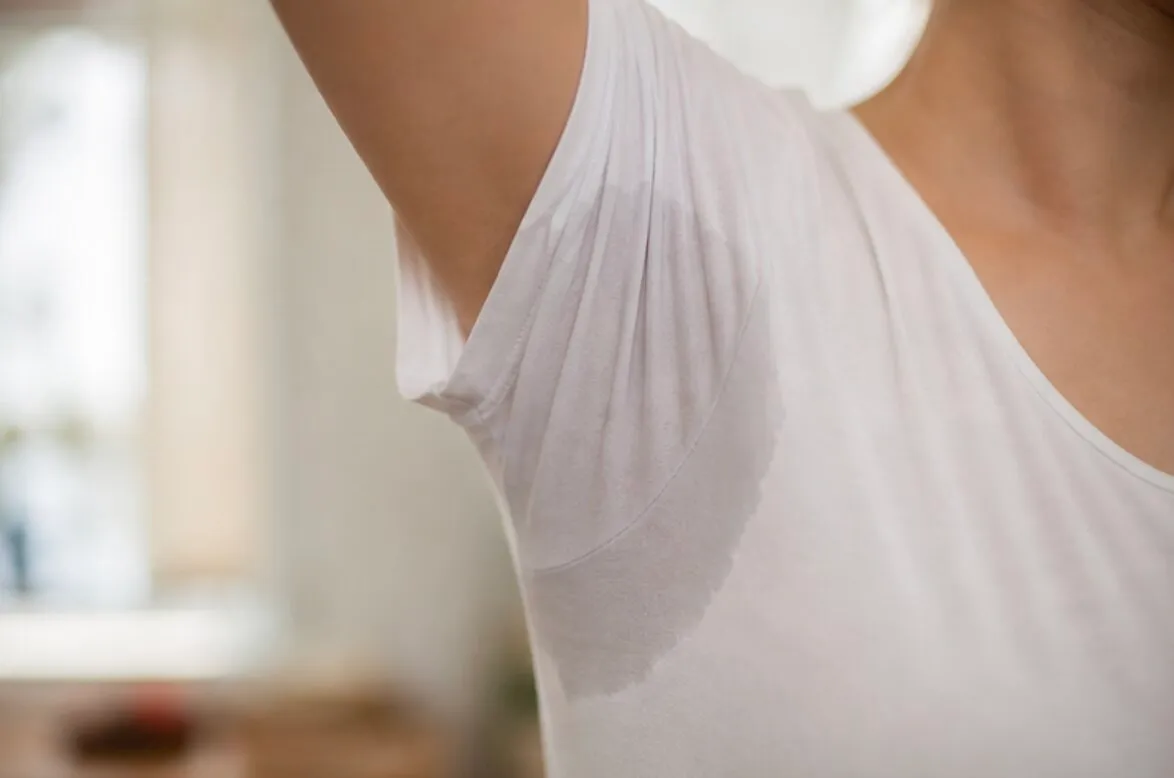 Close-up of a woman's armpit showing a large sweat stain on a white shirt.