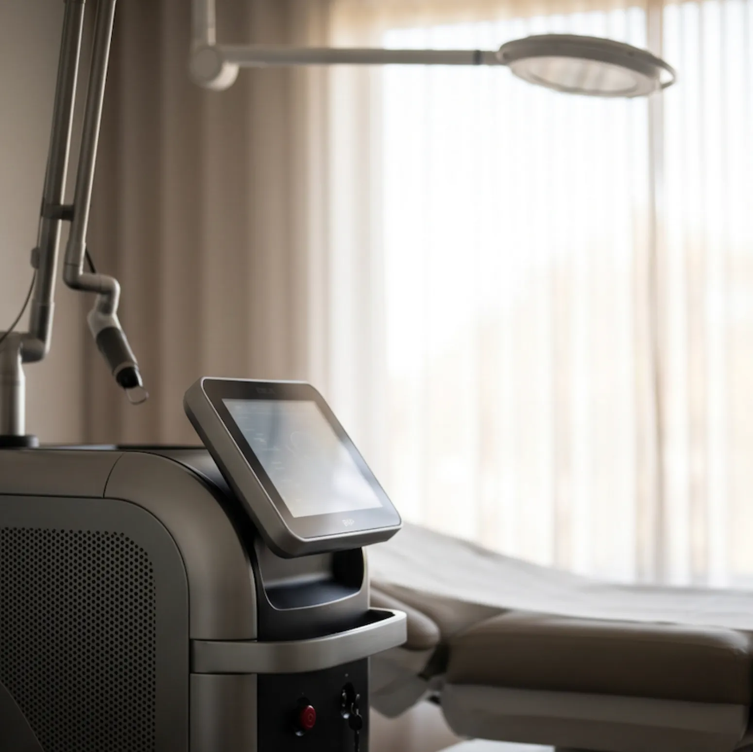 Close-up of a medical laser device with a touchscreen in a softly lit treatment room.