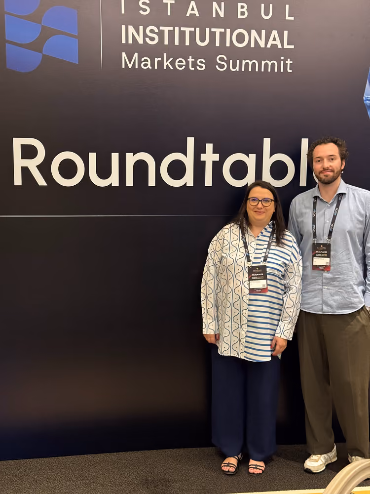 Two people standing in front of a sign that reads Istanbul Institutional Markets Summit Roundtable.