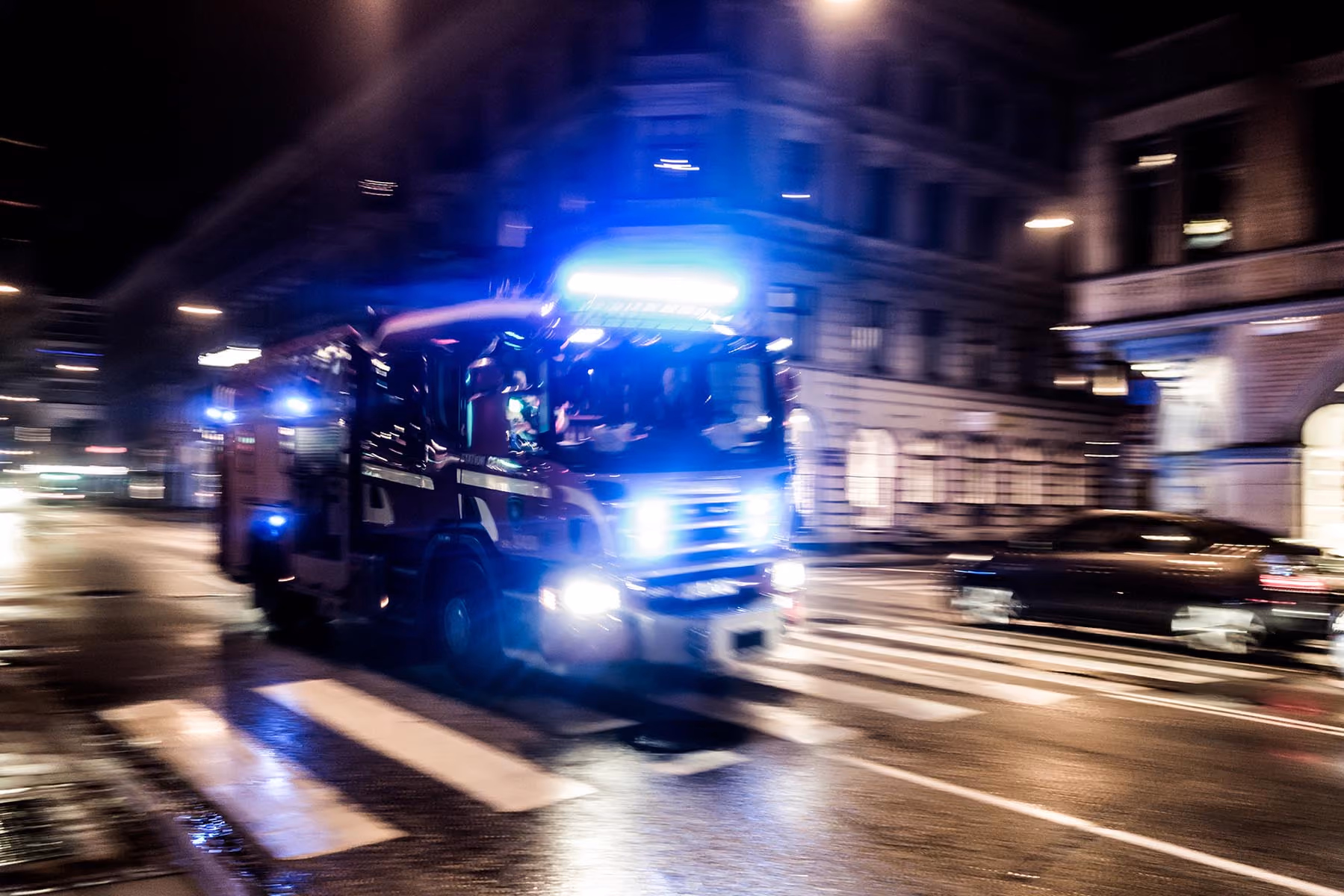 Fire truck with flashing blue lights speeding through a wet city street at night.
