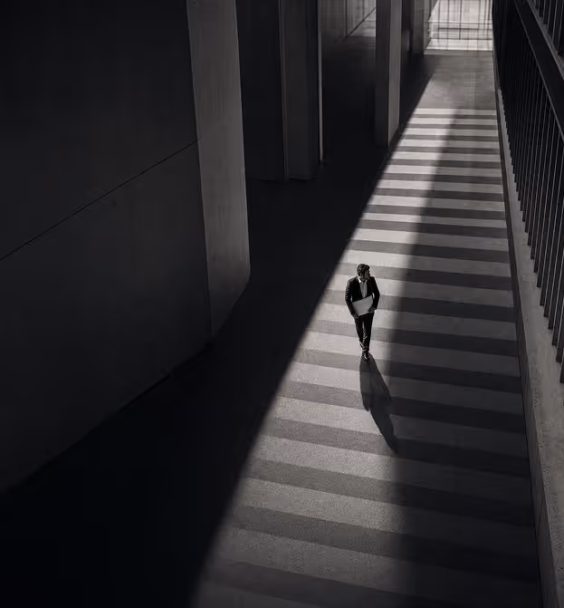 Man in suit walking on striped sunlit floor casting a long shadow in a modern building.