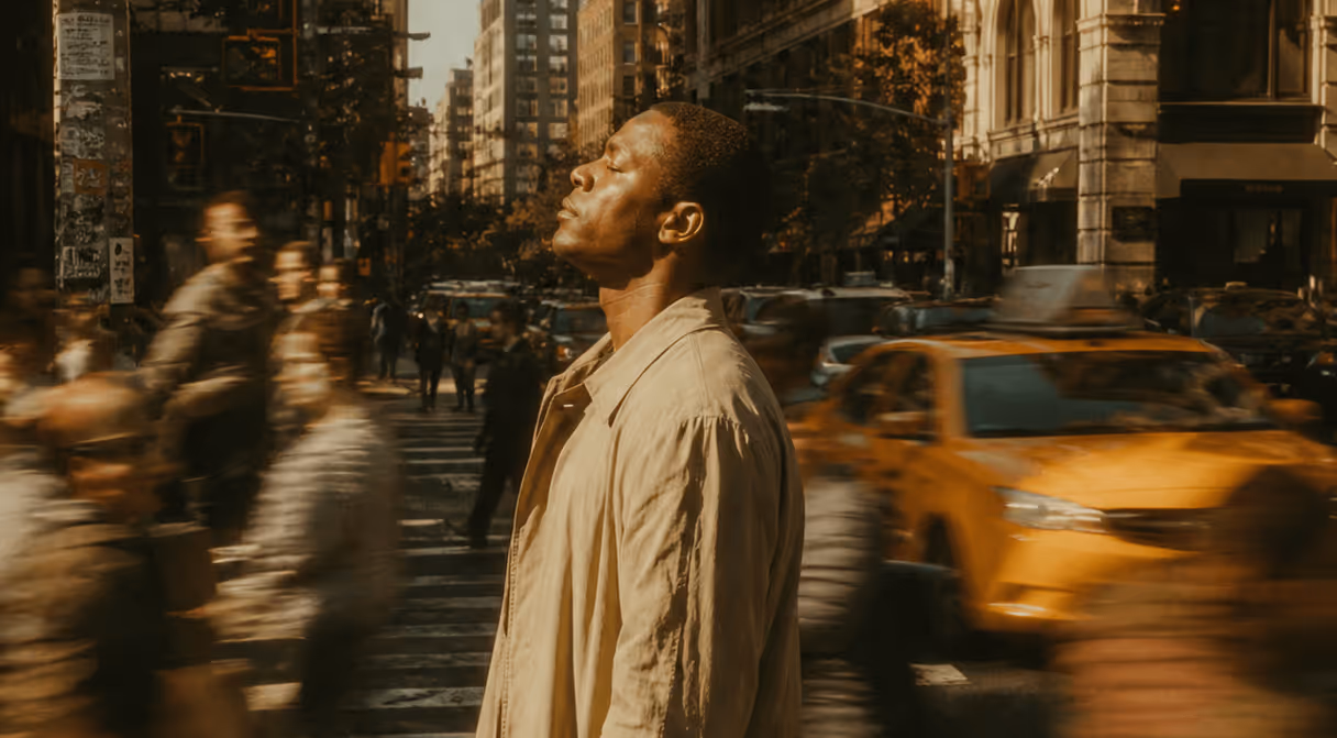 Man in beige coat standing still with eyes closed amid busy blurred city street and yellow taxi.