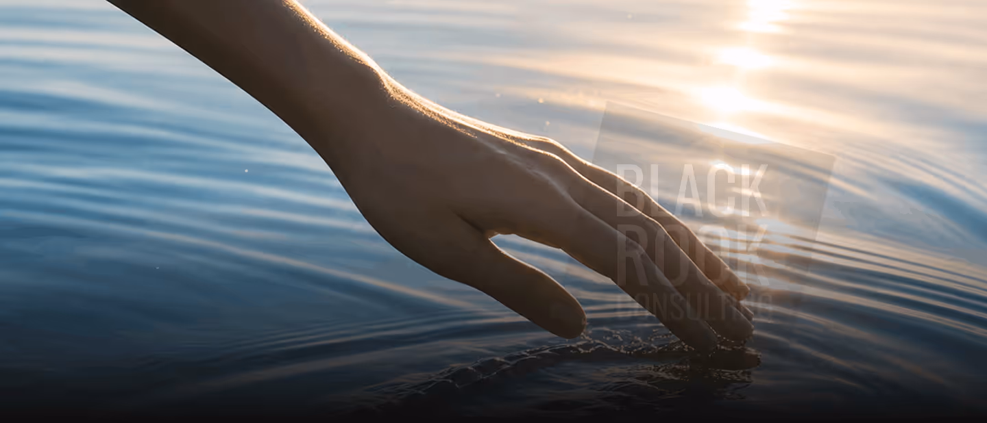 Hand gently touching calm water surface with sunlight reflecting on the ripples.