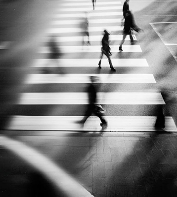 Woman in coat and beanie walking down urban stairs while looking at phone in black and white photo.