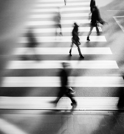 Woman in coat and beanie walking down urban stairs while looking at phone in black and white photo.