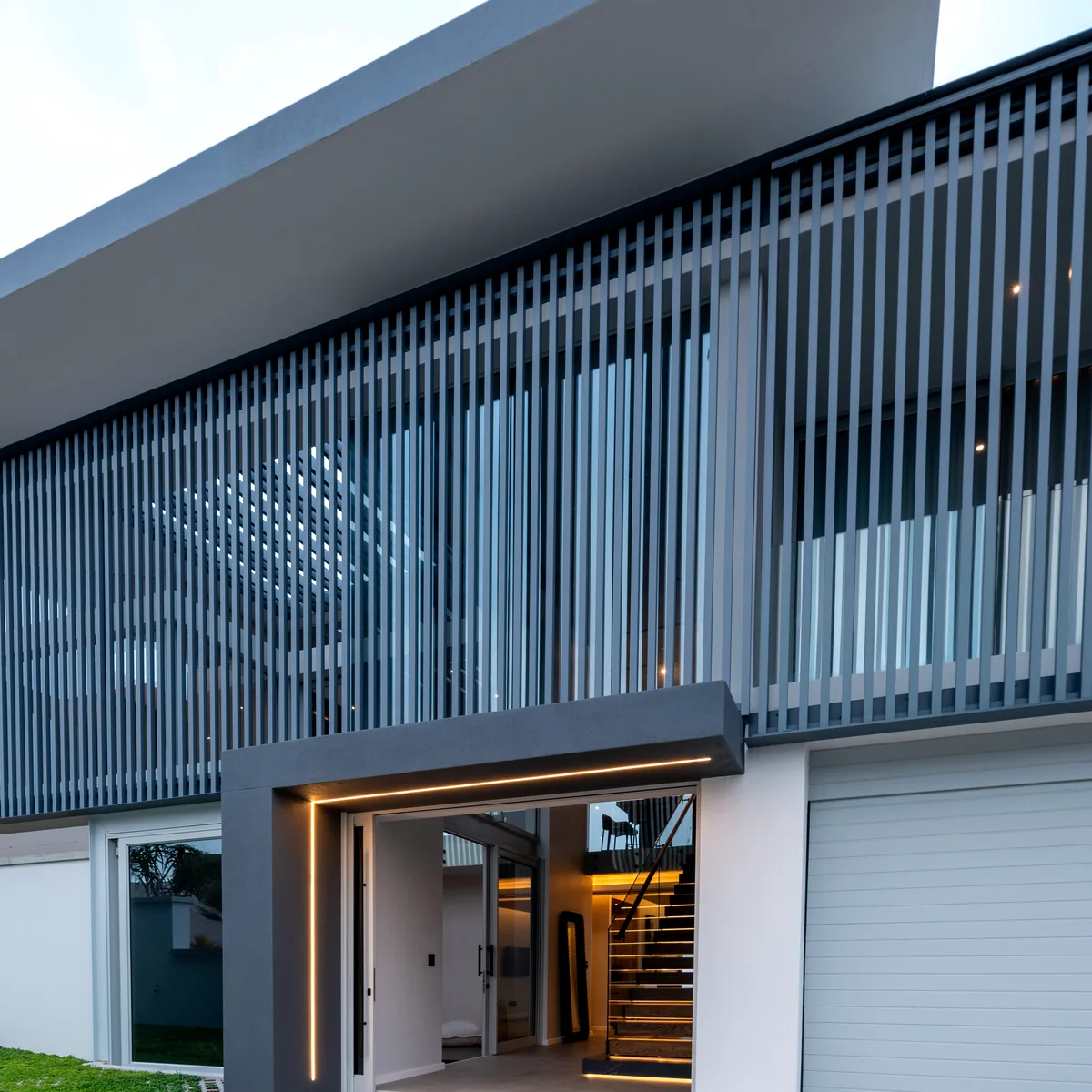 Vertical louvre screening over the lit entrance of a private home at dusk