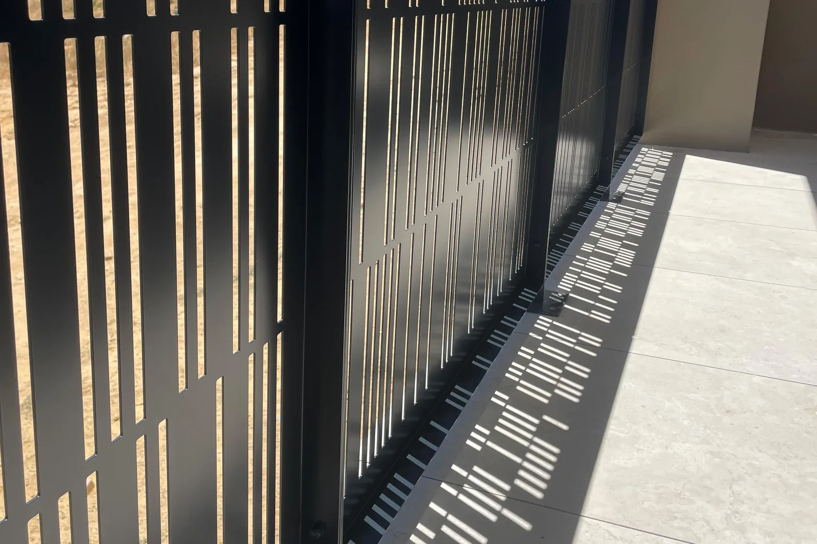 Close-up of slot-pattern perforated aluminium balustrade panels casting shadows on a terrace floor