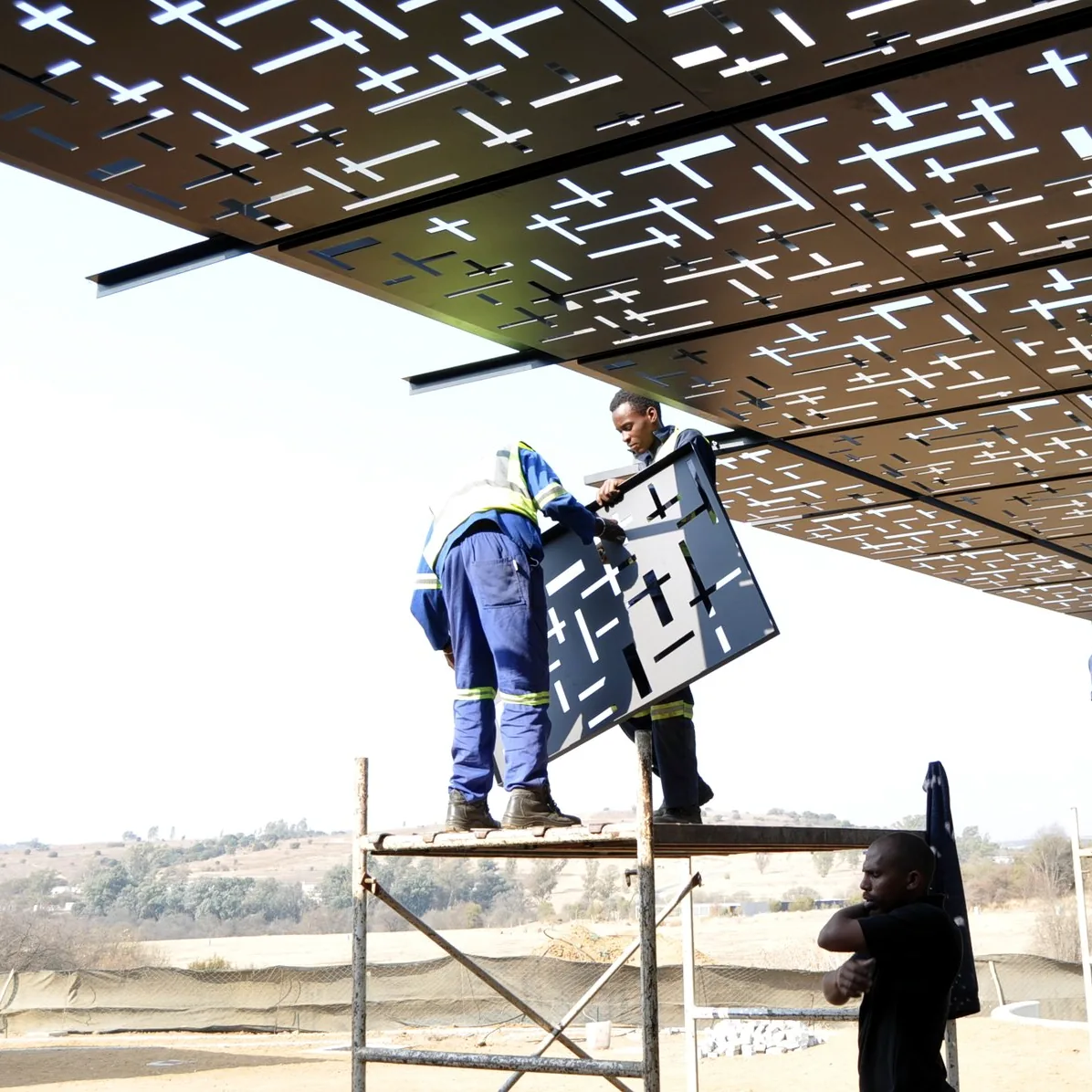 Installers on scaffolding fitting a laser-cut aluminium roof panel to a pergola soffit