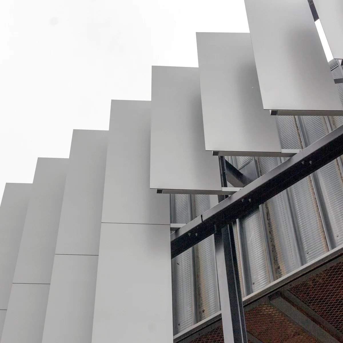 White aluminium fin cladding panels fixed to a facade support frame, close-up of the fixing detail