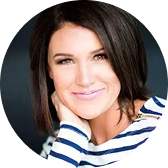 Smiling woman with dark hair resting her head on her hand wearing a striped top.