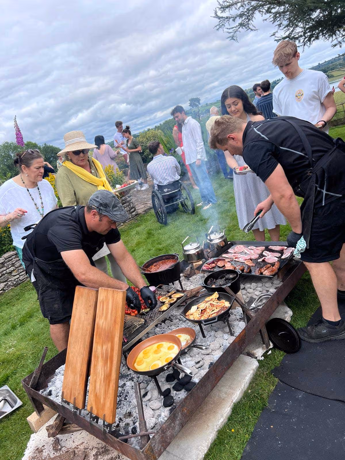 Nyama team grilling meat, eggs, and vegetables on outdoor barbecue at a garden party with guests nearby.