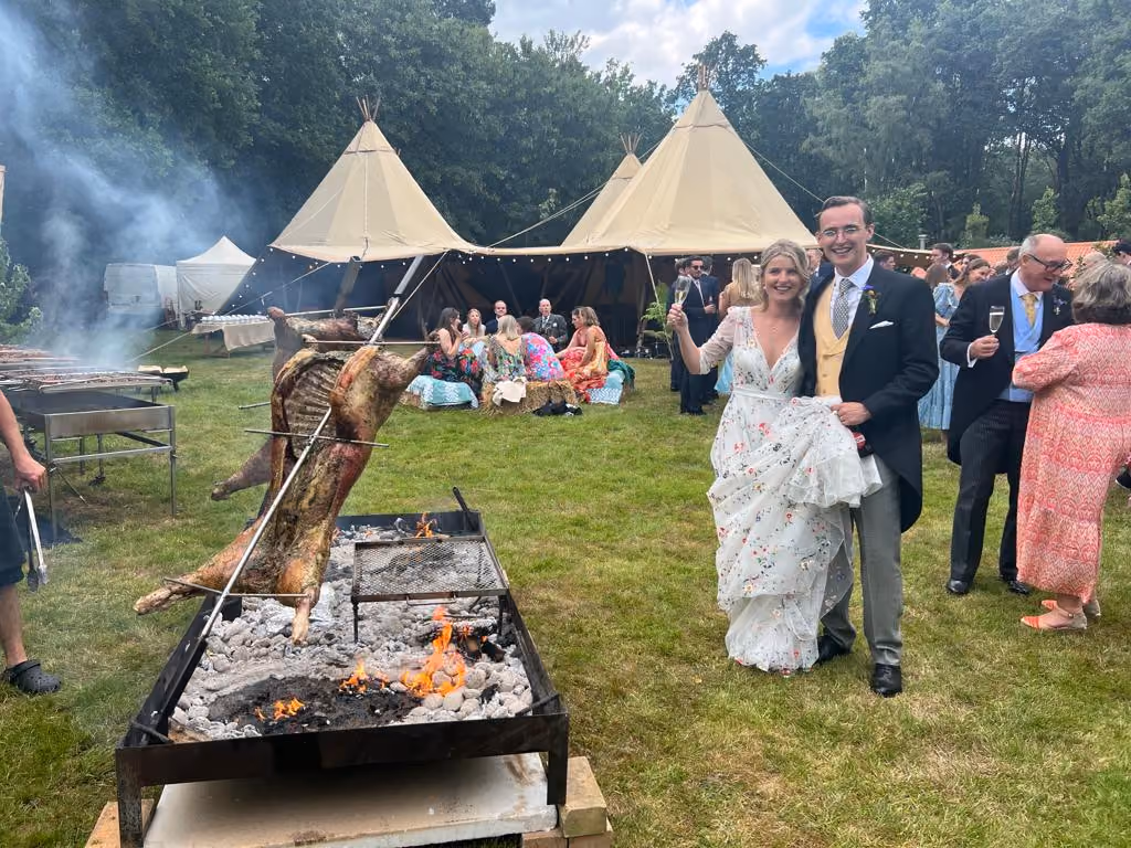 Bride and groom smiling with guests next to an open fire.