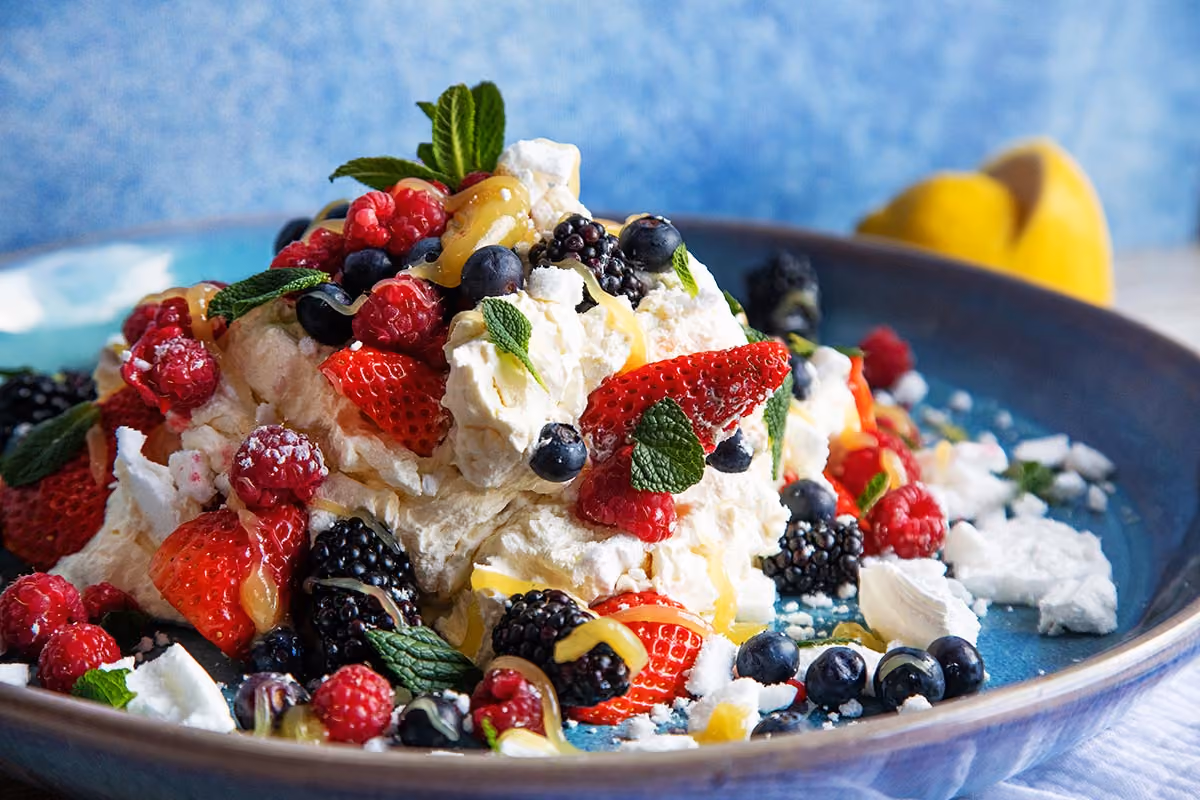 Dessert with whipped cream topped with strawberries, raspberries, blueberries, blackberries, mint leaves, and sauce.