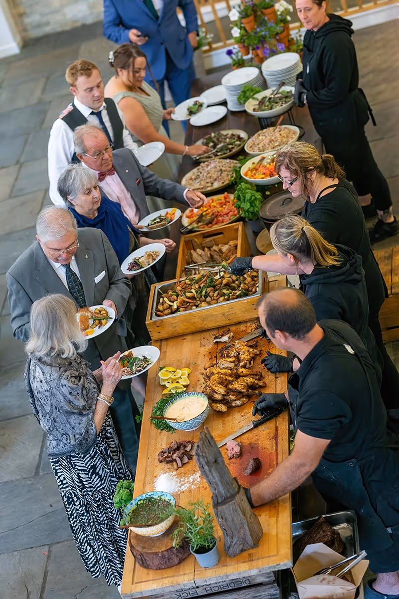 People serving themselves food buffet style from a table with various dishes and servers behind it.